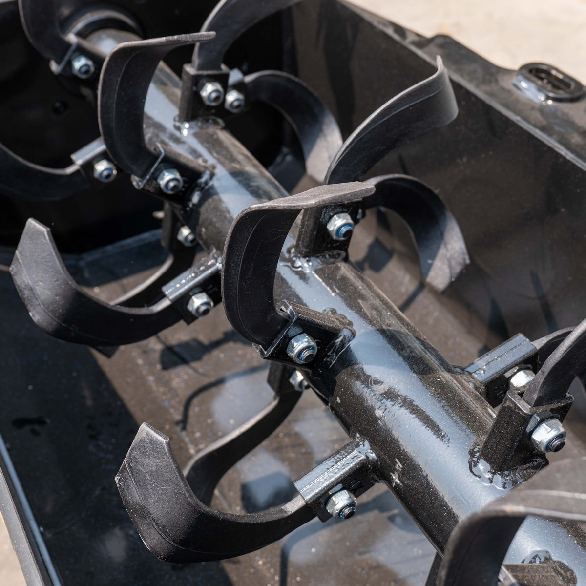 Close-up of black rotary tiller tines and drum for MMS skid steer loader attachment