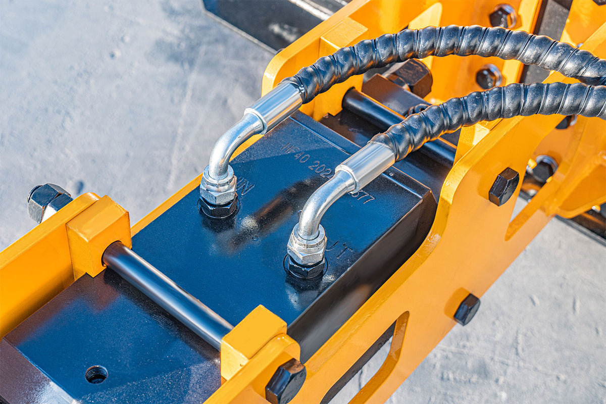 Hydraulic hammer breaker attachment with yellow steel frame and black hydraulic hoses for skid steer