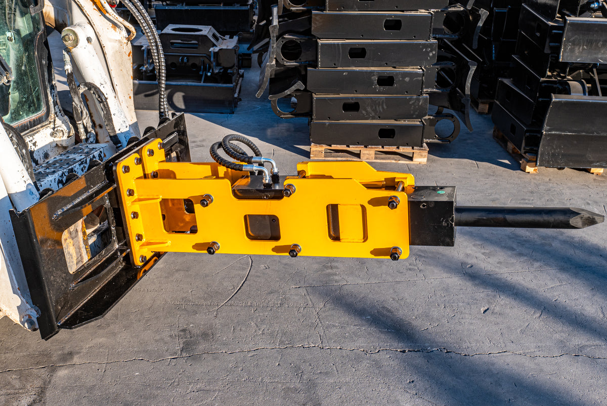 Yellow hydraulic pile driver attachment mounted on a skid steer loader, with black driving ram