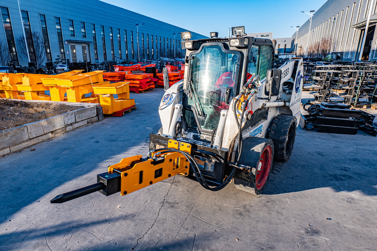 Hydraulic hammer breaker attachment mounted on a skid steer loader, yellow steel housing with chisel